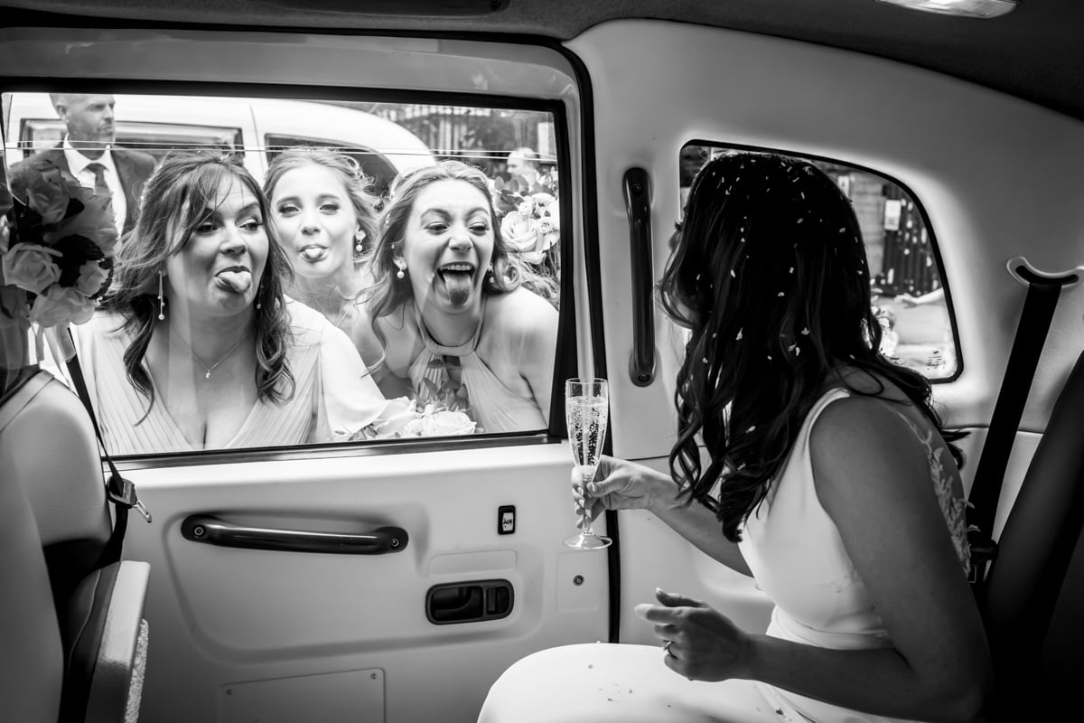 The bridesmaids pull funny faces at the bride in the wedding car