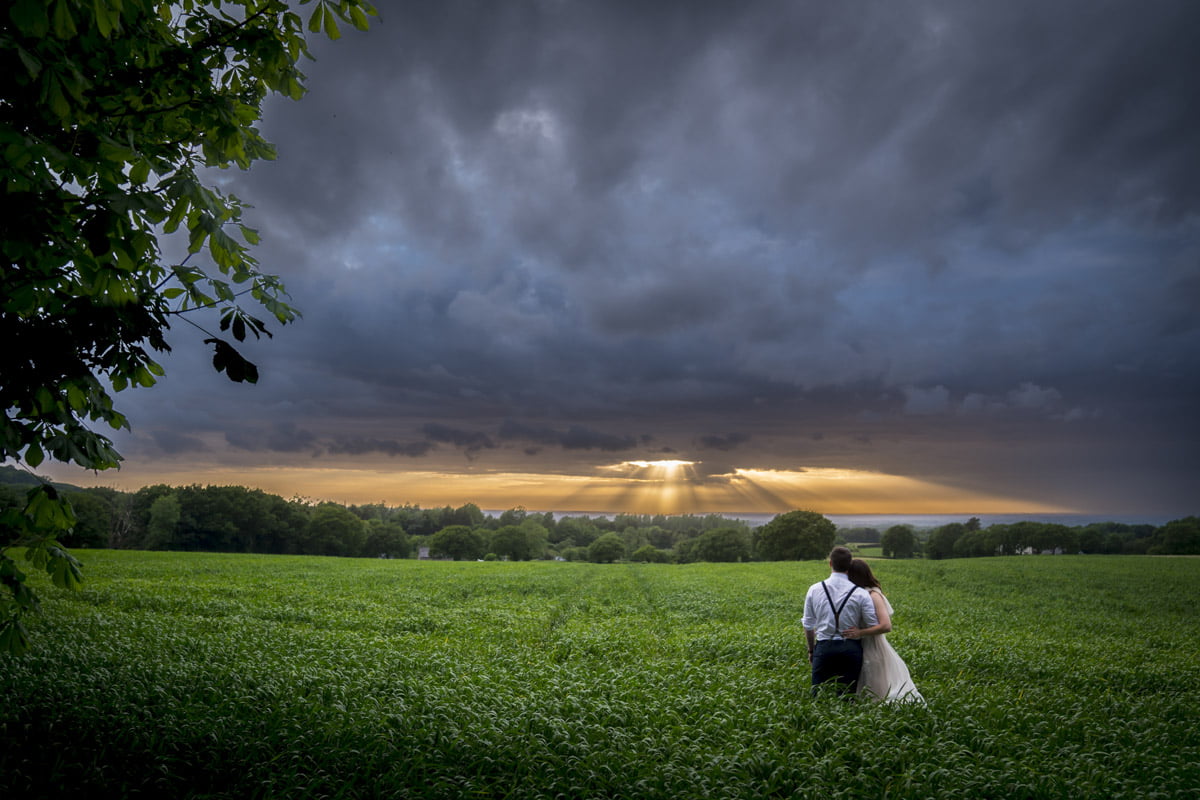 The bride and groom look at the sunset together in the field