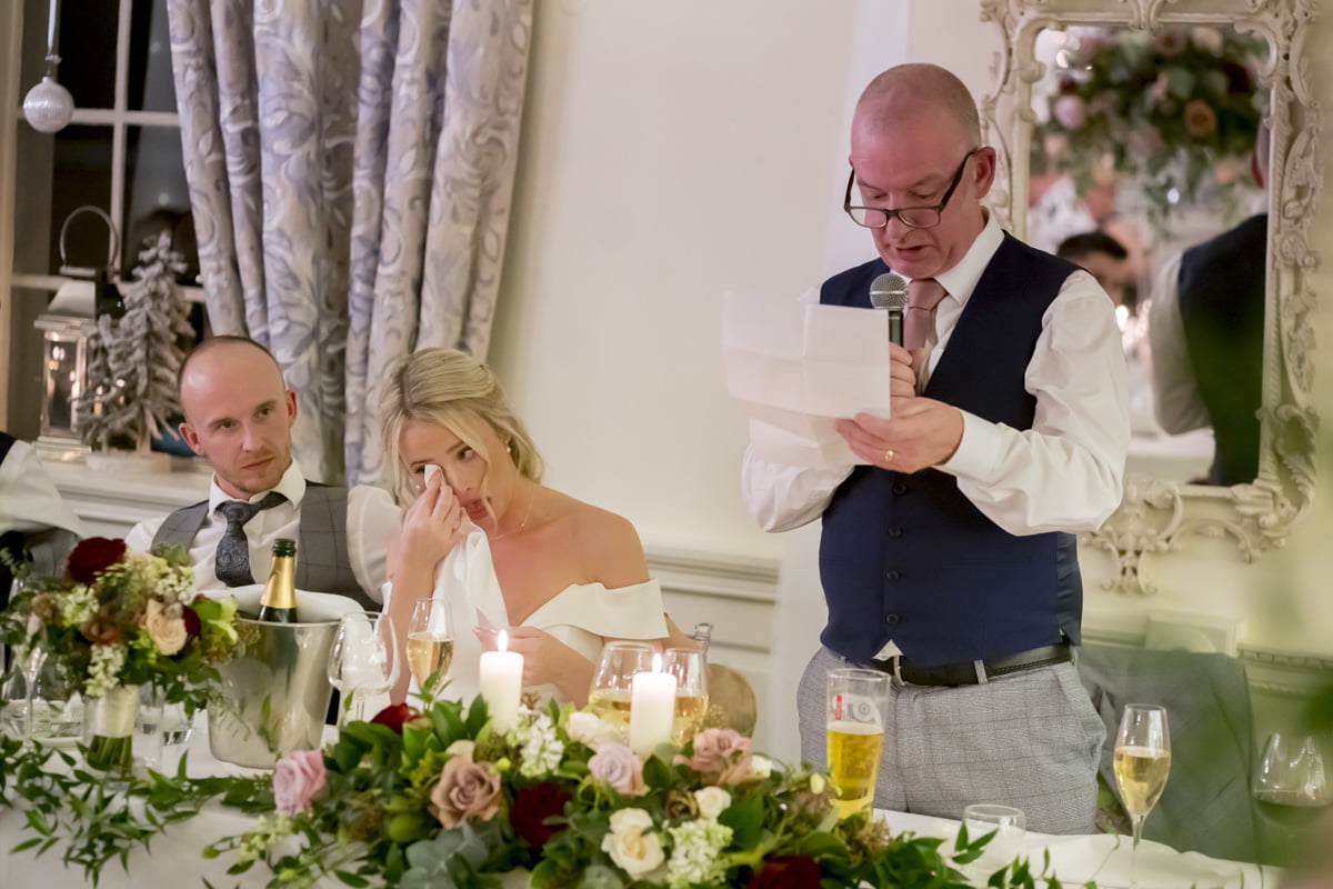 The bride wipes a tear from her eye as her father makes his speech