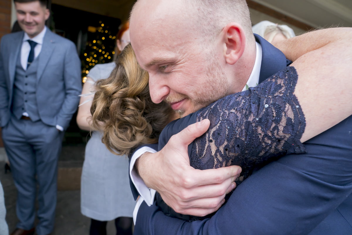 The groom embraces a wedding guest in a hug