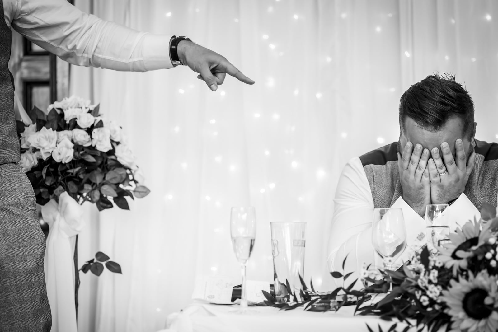 The groom holds his head in his hands as his best man points at him natural wedding photography