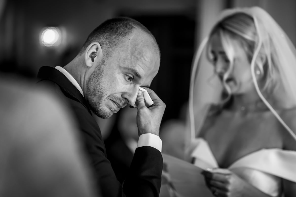 The groom wipes away a tear as the bride reads her vows