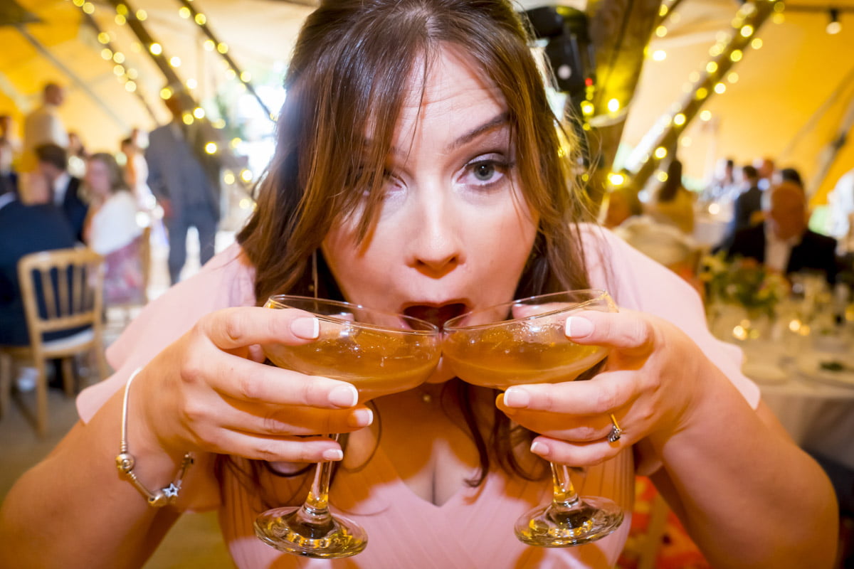 A wedding guest drinks two cocktails at once