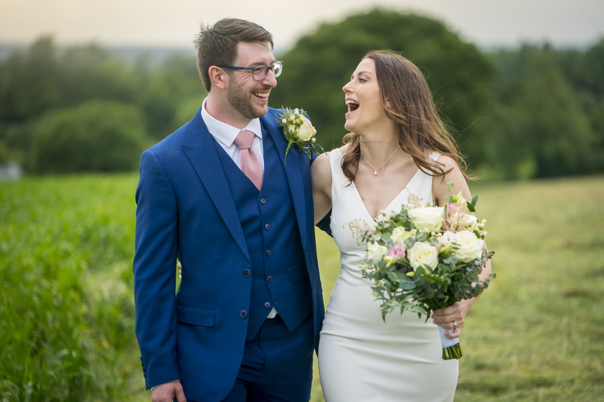 The bride and groom walk through the fields and laugh together