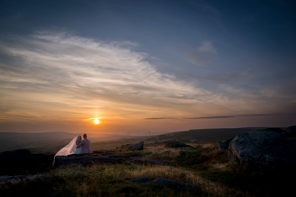 The bride and groom sit together and watch the sun set in this natural portrait
