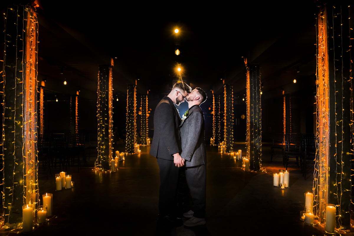 The groom kisses his groom on the forehead in the beautiful fairy lit aisle