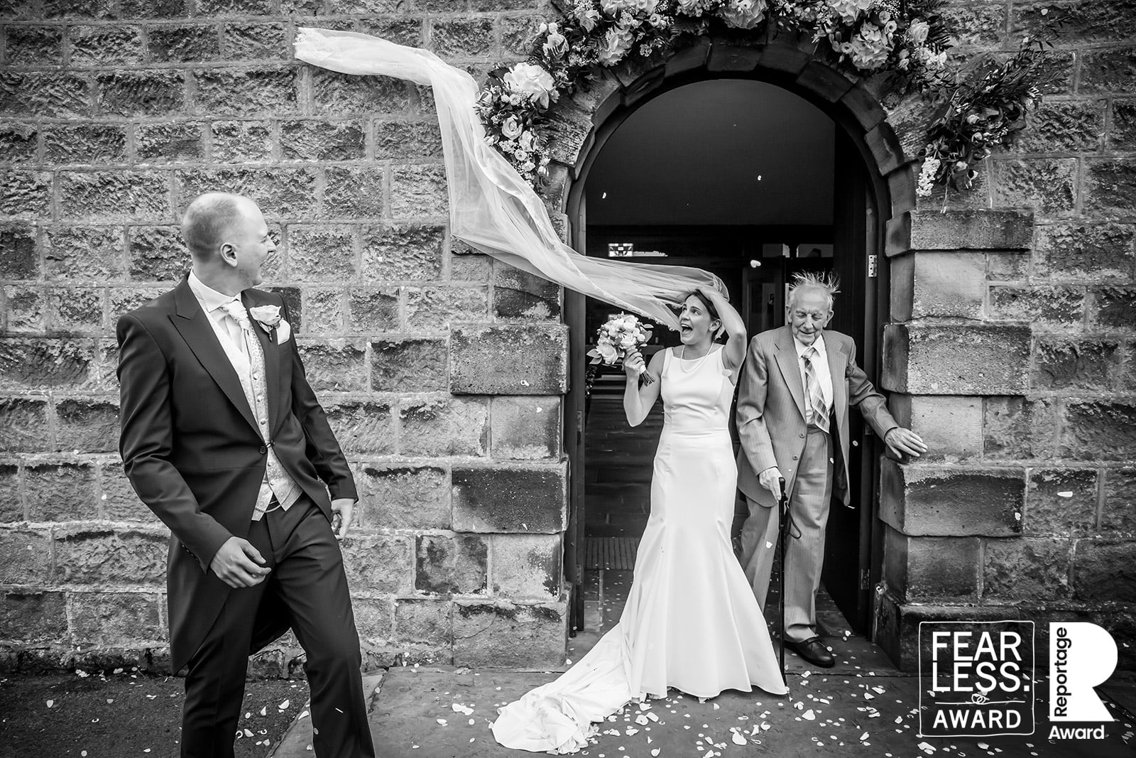 The brides vail is almost swept away by the wind as she exits the church