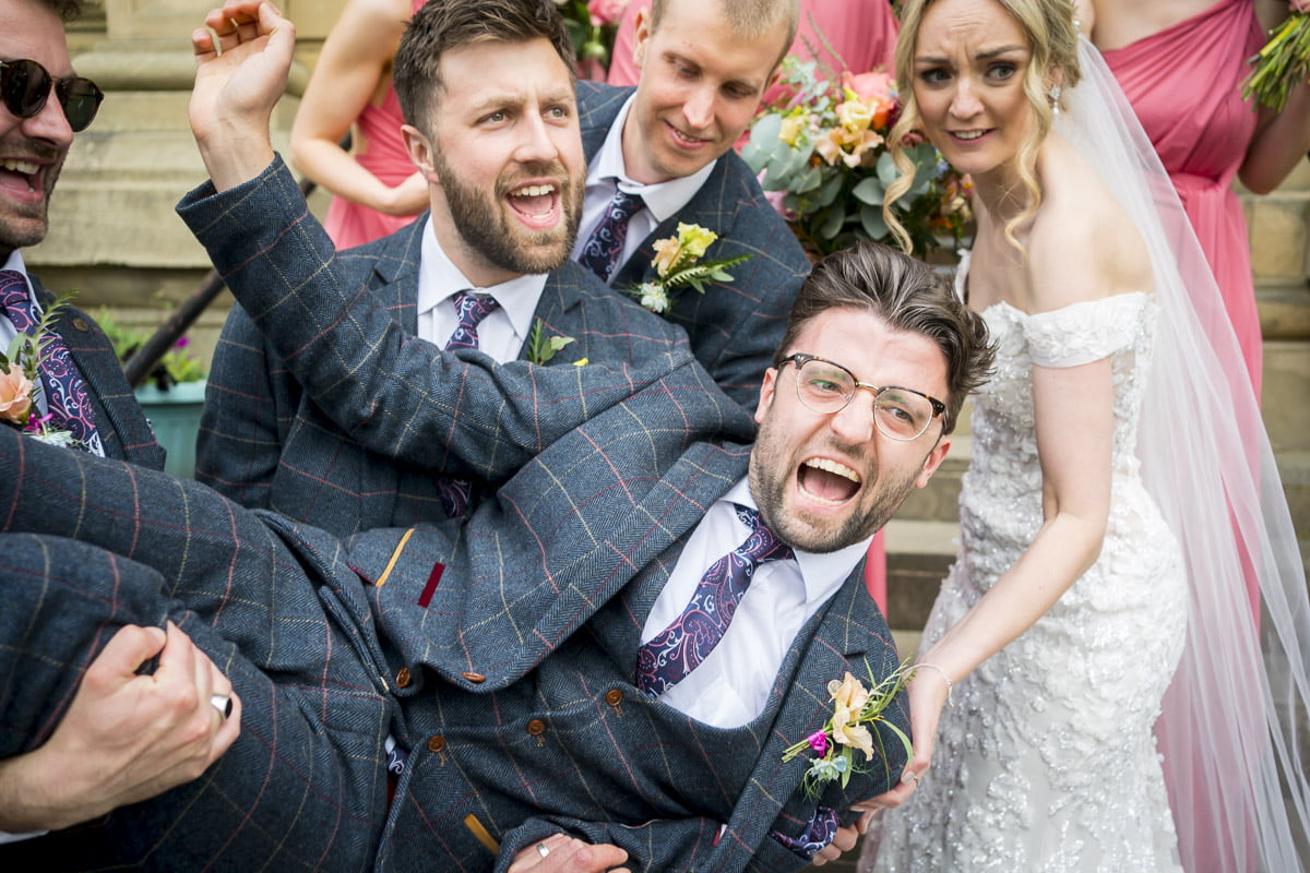 The groom is carried by the wedding party as the bride looks on confused
