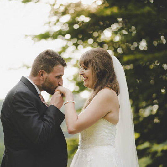 The groom kisses his brides hand in the beautiful landscape